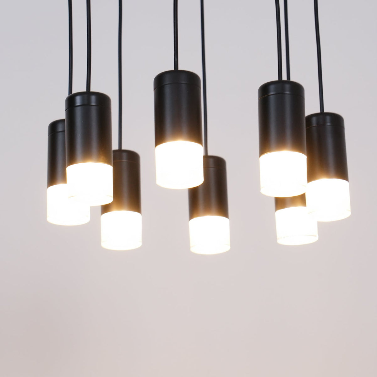 Close view of lit black light heads with glowing white diffusers at different heights on this Clérachic pendant.