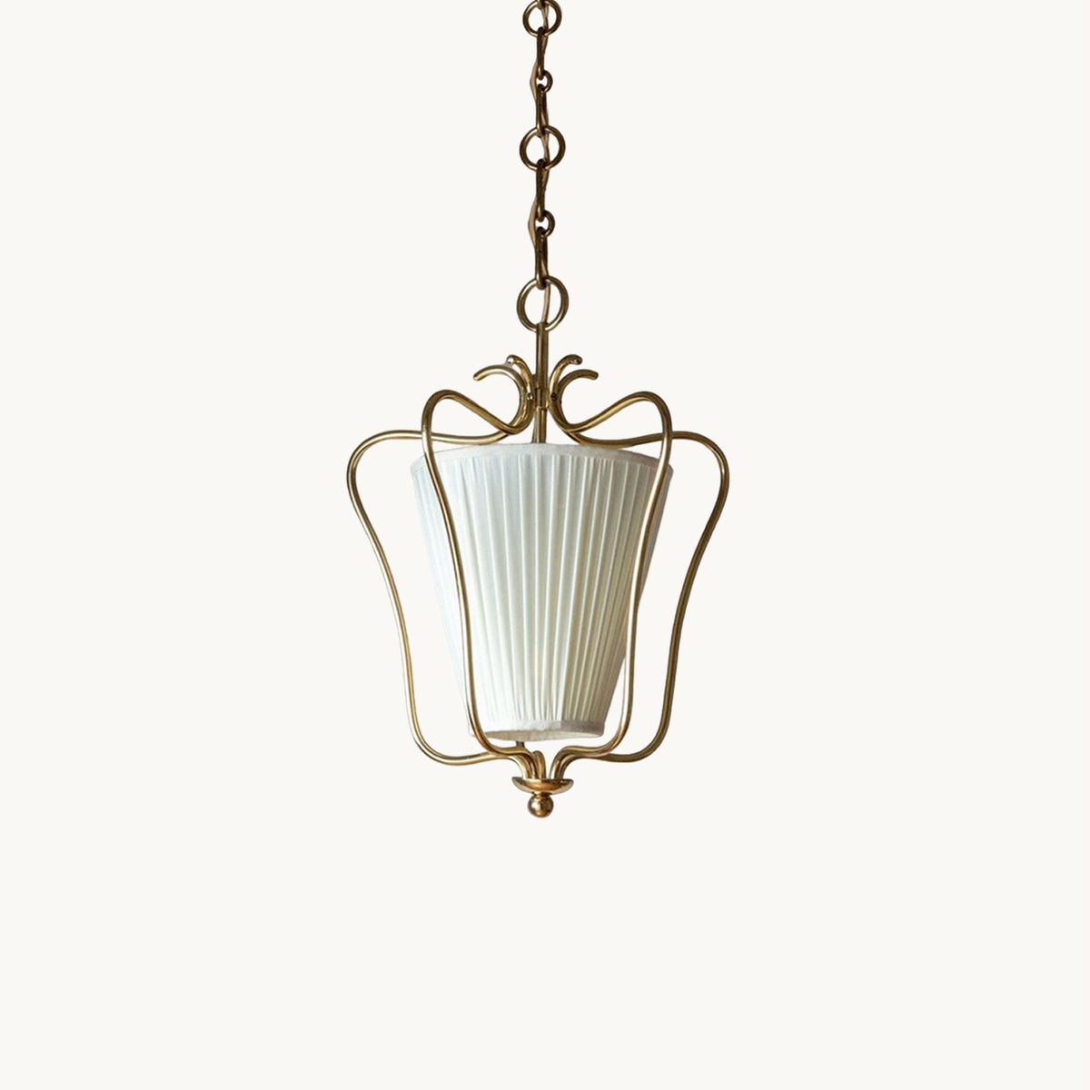 Clérachic brass lantern pendant with a vertically pleated white fabric shade inside a curled wire frame, on a plain white backdrop.