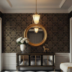 Lit Clérachic brass pendant hanging above a gilt round mirror and a mirrored black console, against black and gold damask wallpaper.