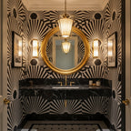 Clérachic pendant beside a round gold mirror in a bathroom with black-and-white sunburst wallpaper and a black marble vanity.