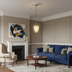 This Clérachic brass pendant hangs from a ceiling rose in a living room with a navy sofa, a marble fireplace and an abstract painting.