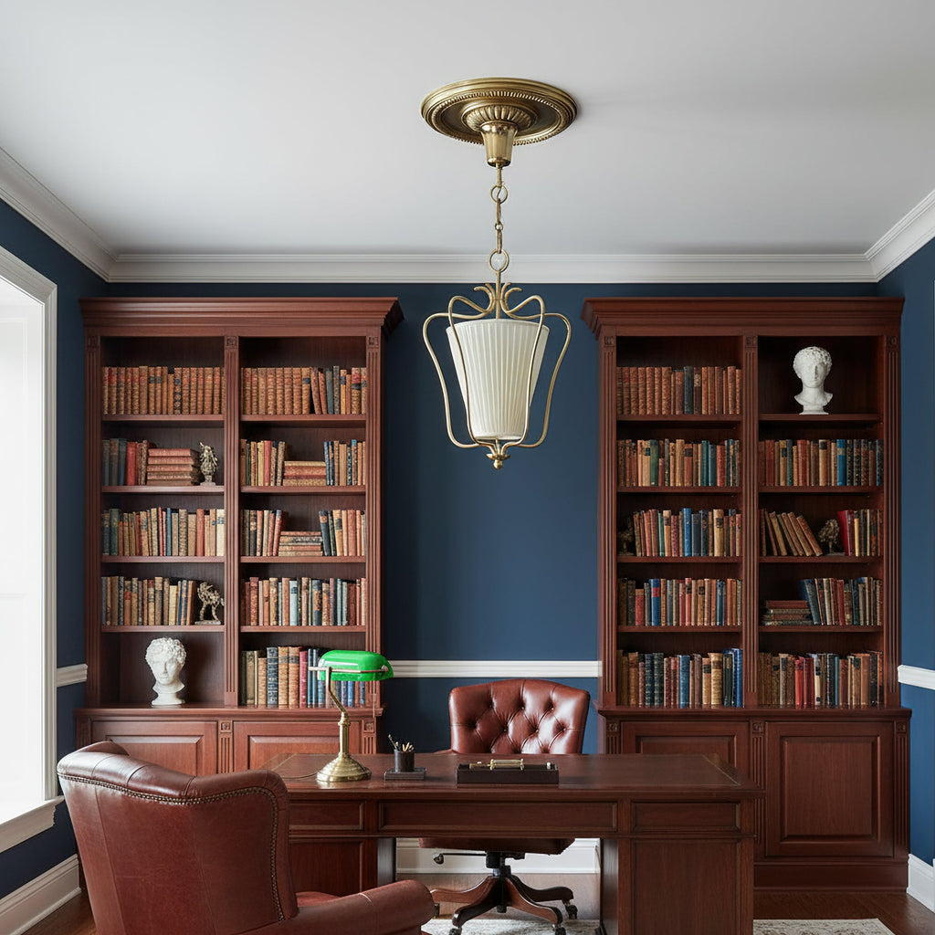 Clérachic brass pendant in a study with navy walls, two tall wooden bookcases and a green-shaded desk lamp.