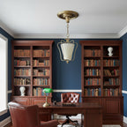 Clérachic brass pendant in a study with navy walls, two tall wooden bookcases and a green-shaded desk lamp.