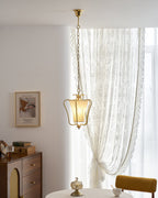 Clérachic pendant with a diagonal-pleat shade beside a sheer curtain, with a walnut sideboard and a framed print below.