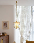 Clérachic brass lantern pendant with a twisted fabric shade in front of a lace curtain, with a small glass dish at the bottom.