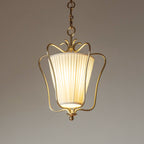 Glowing Clérachic pendant with a vertically pleated shade inside the brass frame, against a warm taupe backdrop.