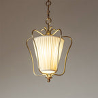 Close view of a lit Clérachic brass pendant with a vertically pleated shade and a curled crown, on a taupe backdrop.