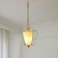 Lit Clérachic brass pendant with a pleated shade, hanging from a chain beside a white cornice and a curtain edge.