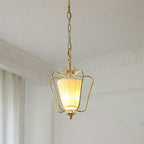 Lit Clérachic brass pendant with a pleated shade, hanging from a chain beside a white cornice and a curtain edge.