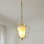 Clérachic pendant on a brass chain with a vertically pleated shade glowing, below white ceiling mouldings.