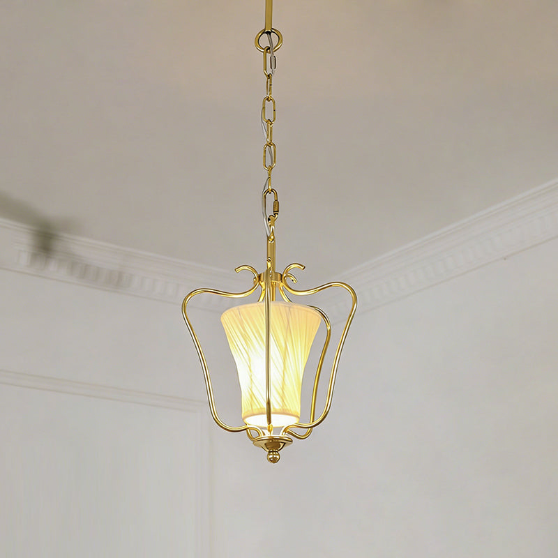 Lit Clérachic brass pendant with a diagonally pleated shade, hanging below white ceiling mouldings.