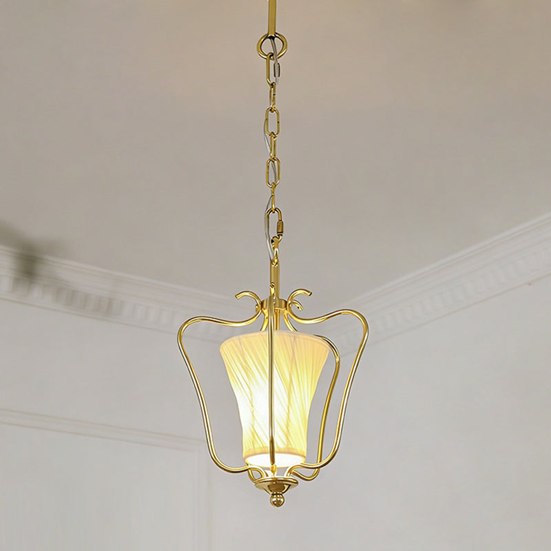 Clérachic brass pendant with a glowing twisted-pleat shade, hung from a chain beneath a white cornice.