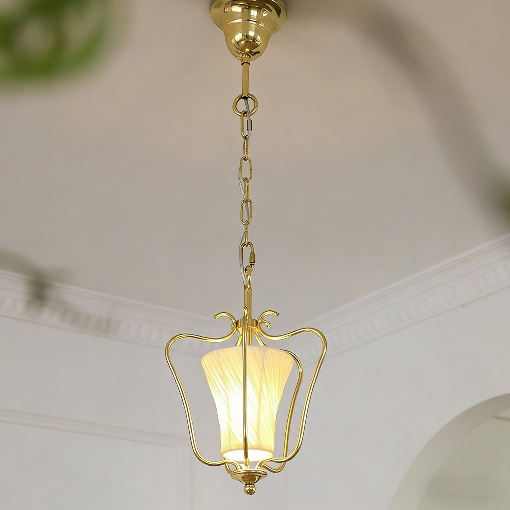 Clérachic brass pendant with a glowing diagonal-pleat shade, below a white cornice and a curved doorway.
