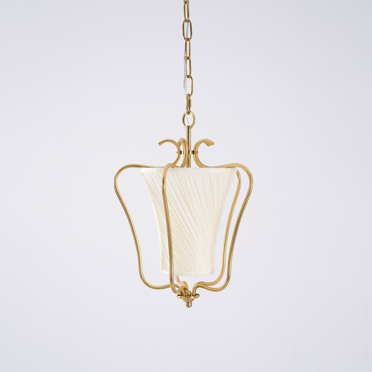 Clérachic brass pendant with a cream twisted-pleat shade and a curled crown, on a pale lilac-grey backdrop.