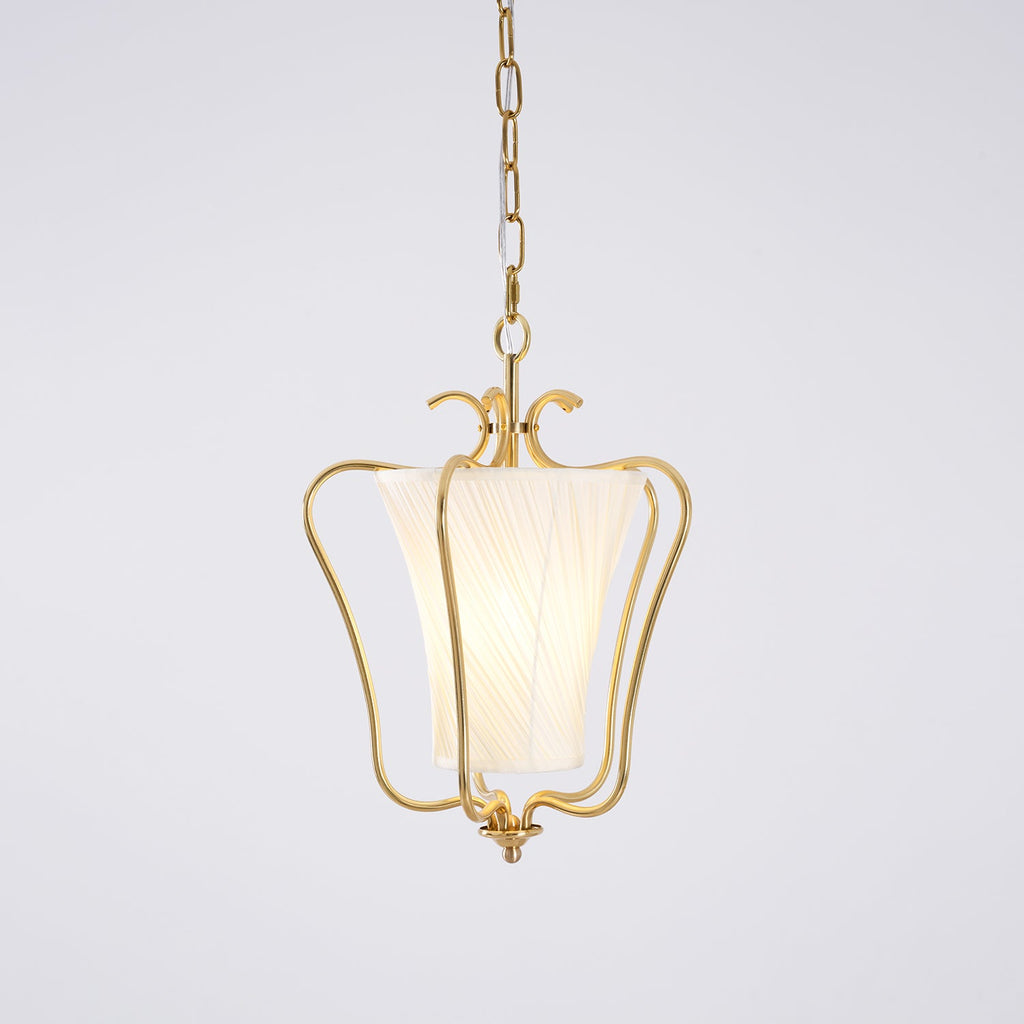 Clérachic pendant with a lit diagonally pleated shade inside the brass frame, on a pale lilac-grey backdrop.