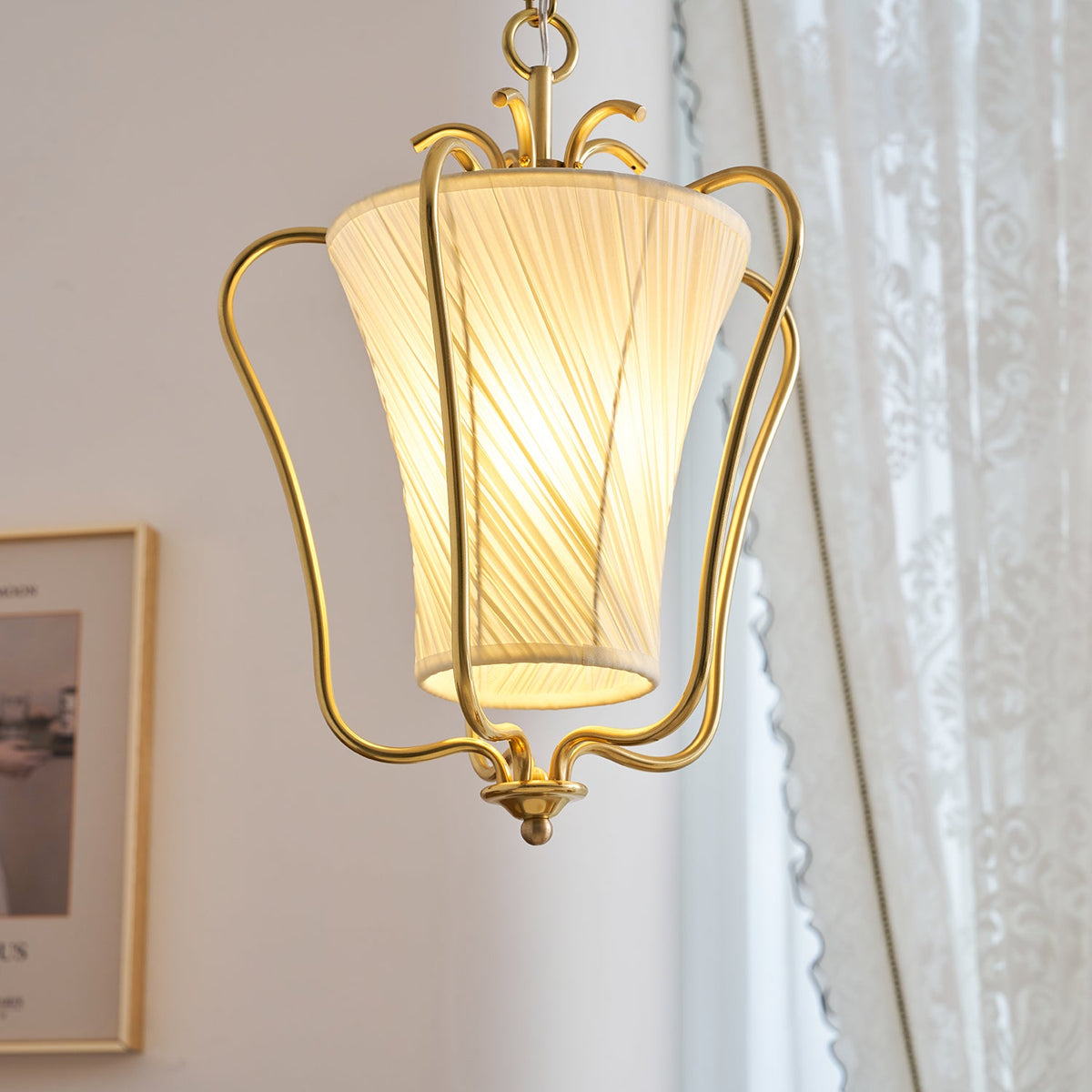 Close view of the glowing diagonal pleats on this Clérachic pendant, with a lace curtain and a framed print behind.