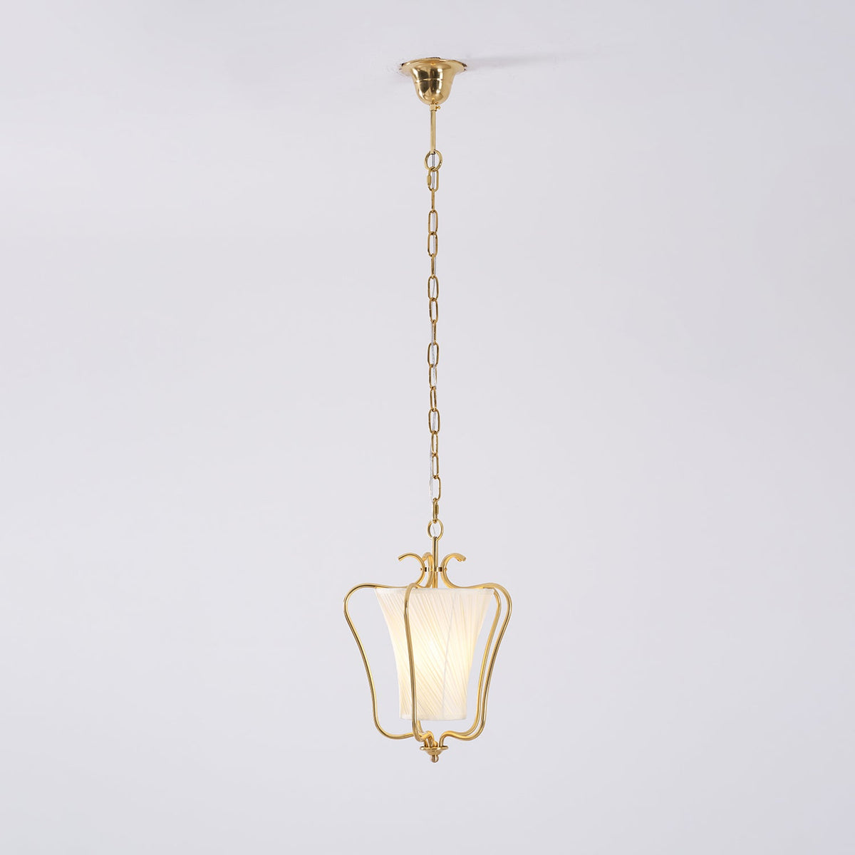 Clérachic pendant on its slim brass chain and ceiling canopy, with a twisted-pleat shade, on a pale backdrop.