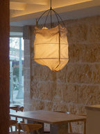 Beside a sunlit window and a stone wall, this Clérachic pendant hangs lit above a dining table.