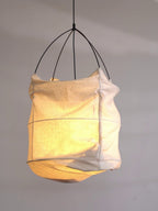 Close view of the beige fabric shade and curved wire ribs on this Clérachic pendant, lit against a plain grey wall.