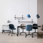 Two blue-shaded Clérachic pendants over a table with navy and grey chairs, against a white wall with wall shelves.