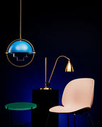 Blue Clérachic pendant in a thin gold ring above a desk lamp and a pink chair, on a deep navy backdrop.