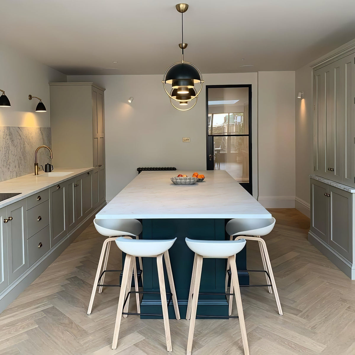 Black Clérachic pendant with brass details over a long white kitchen island with pale bar stools.