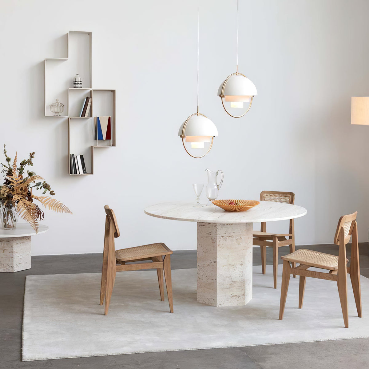 Two white Clérachic pendants with gold rings above a round stone table, beside a wall shelf and a floor lamp.