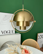 Gold-toned Clérachic pendant above a round table with a vase of dried flowers, against a green wall and a framed poster.
