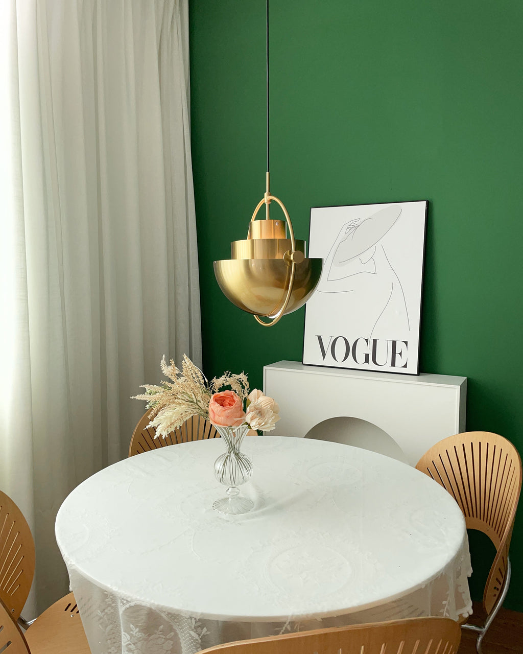 Gold-toned Clérachic pendant with its shade halves partly open, above a round white table and a small flower arrangement.