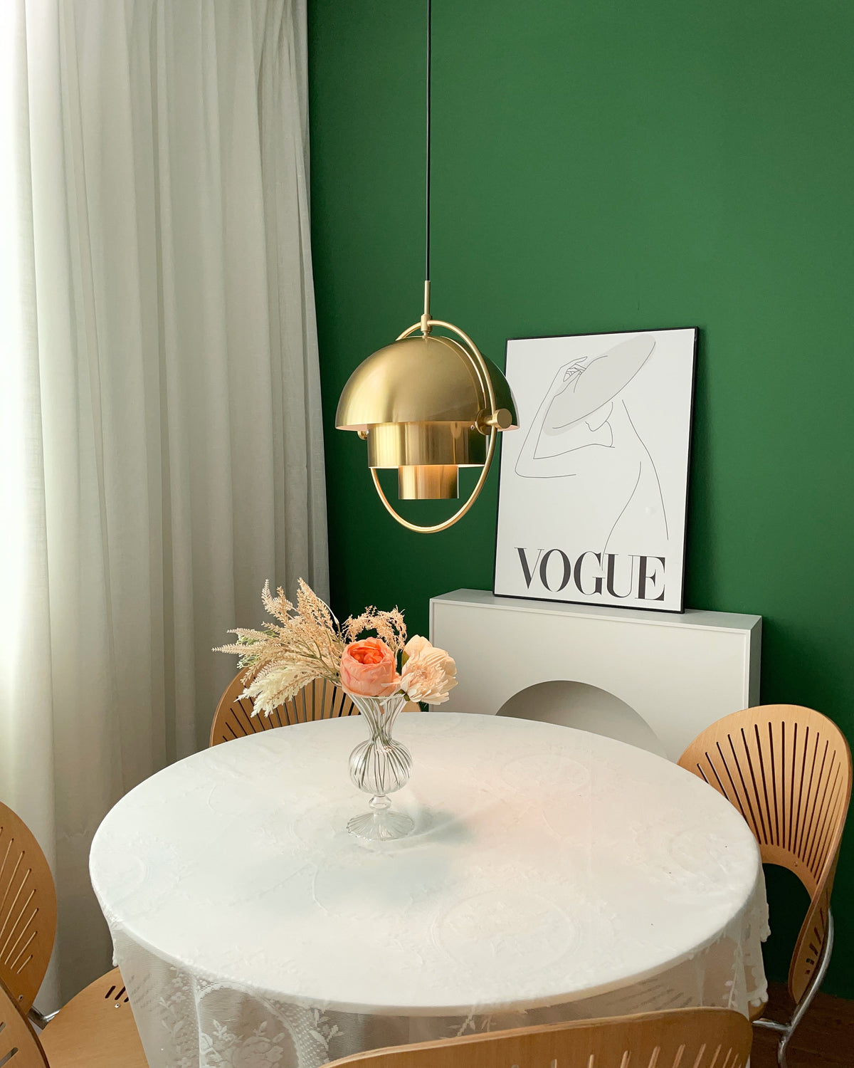 Small view of a gold-toned Clérachic pendant with a gold ring, above a round white table and a green wall.