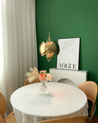 Gold-toned Clérachic pendant with its shade halves swung sideways, above a round table, a vase and a framed poster.
