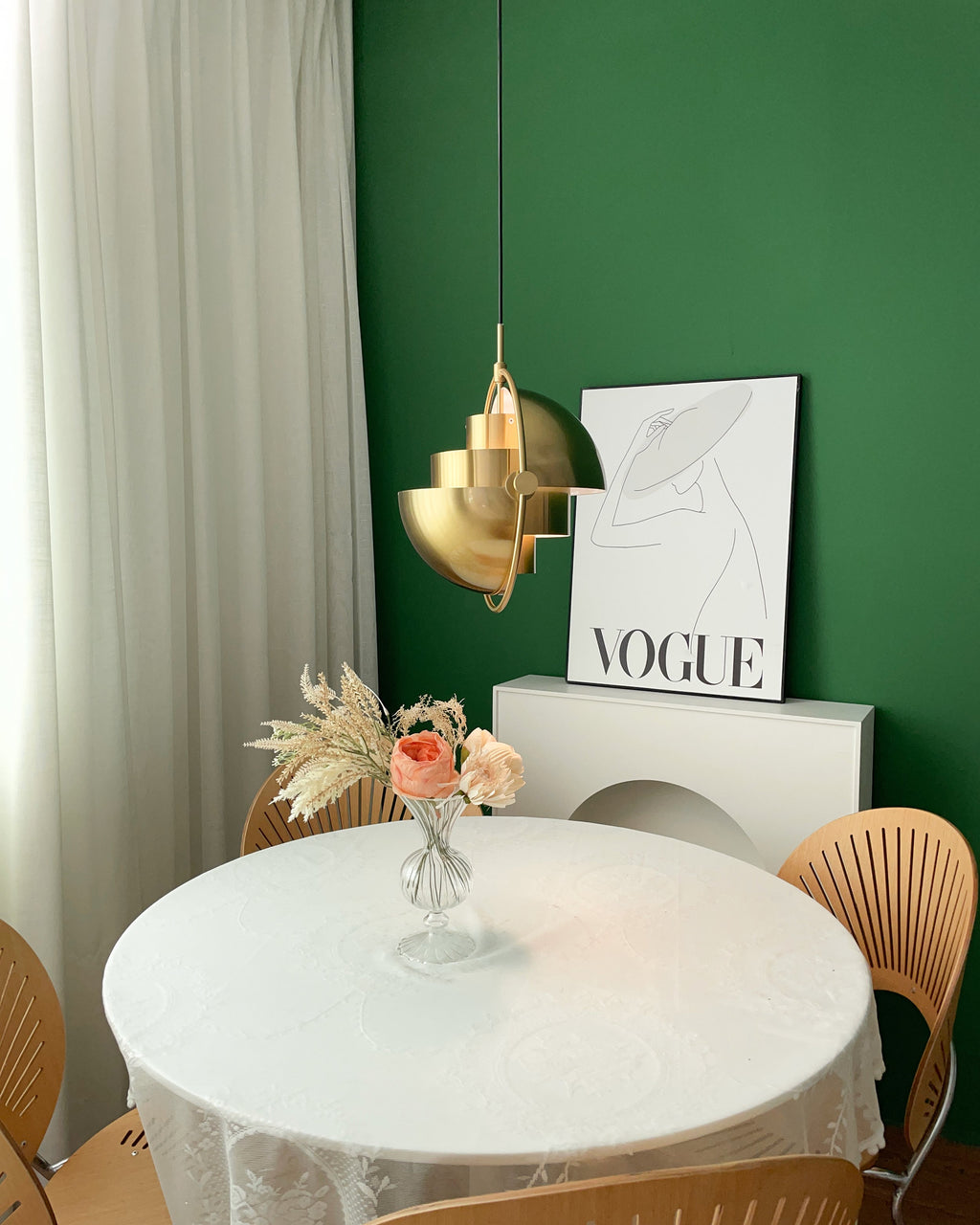 Gold-toned Clérachic pendant with its stepped layers turned towards the viewer, beside a framed poster on a green wall.
