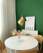 Gold-toned Clérachic pendant with its stepped layers turned towards the viewer, beside a framed poster on a green wall.