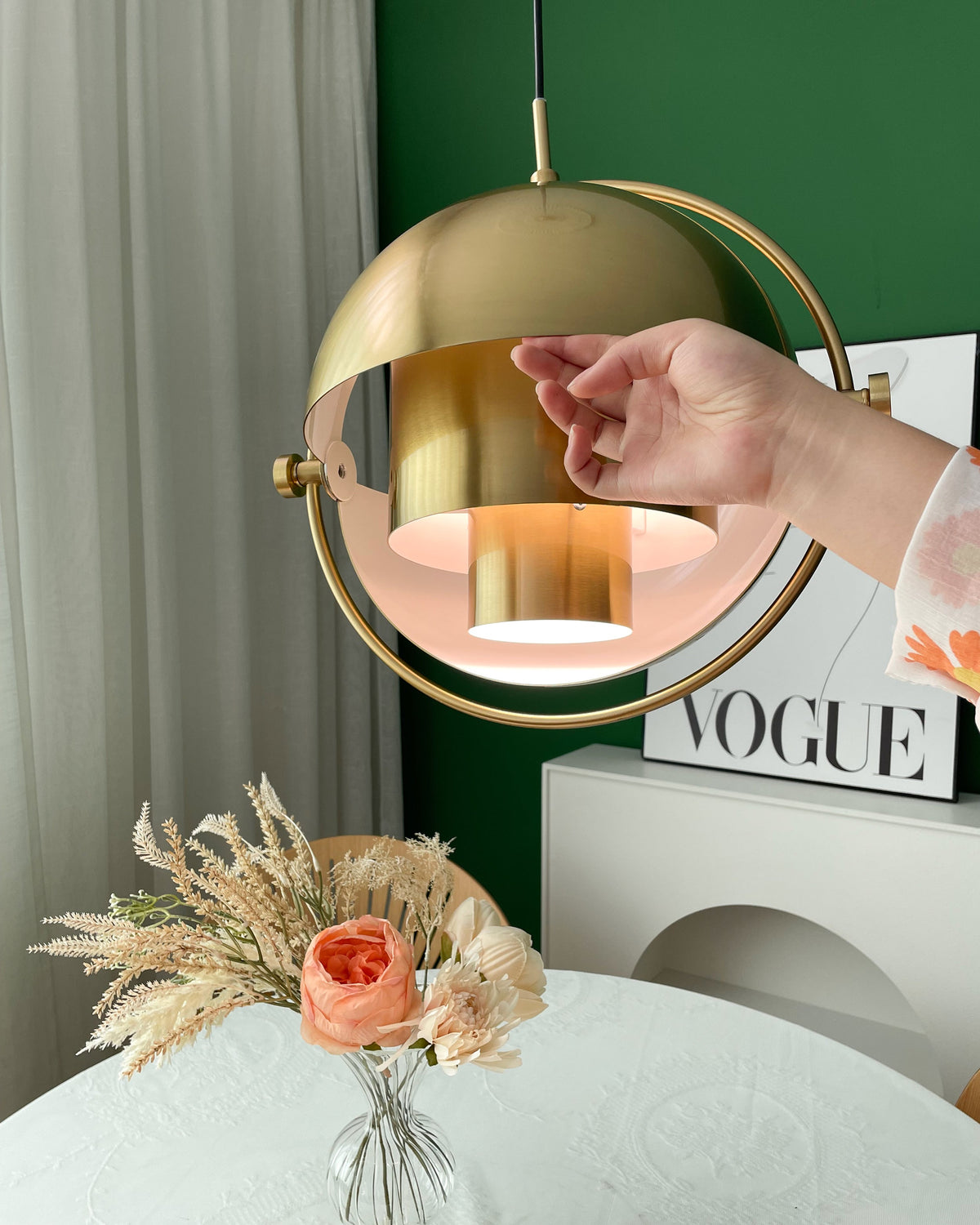A hand tilts the gold-toned shade of this Clérachic pendant open to show the inner cylinder and a white inner face.