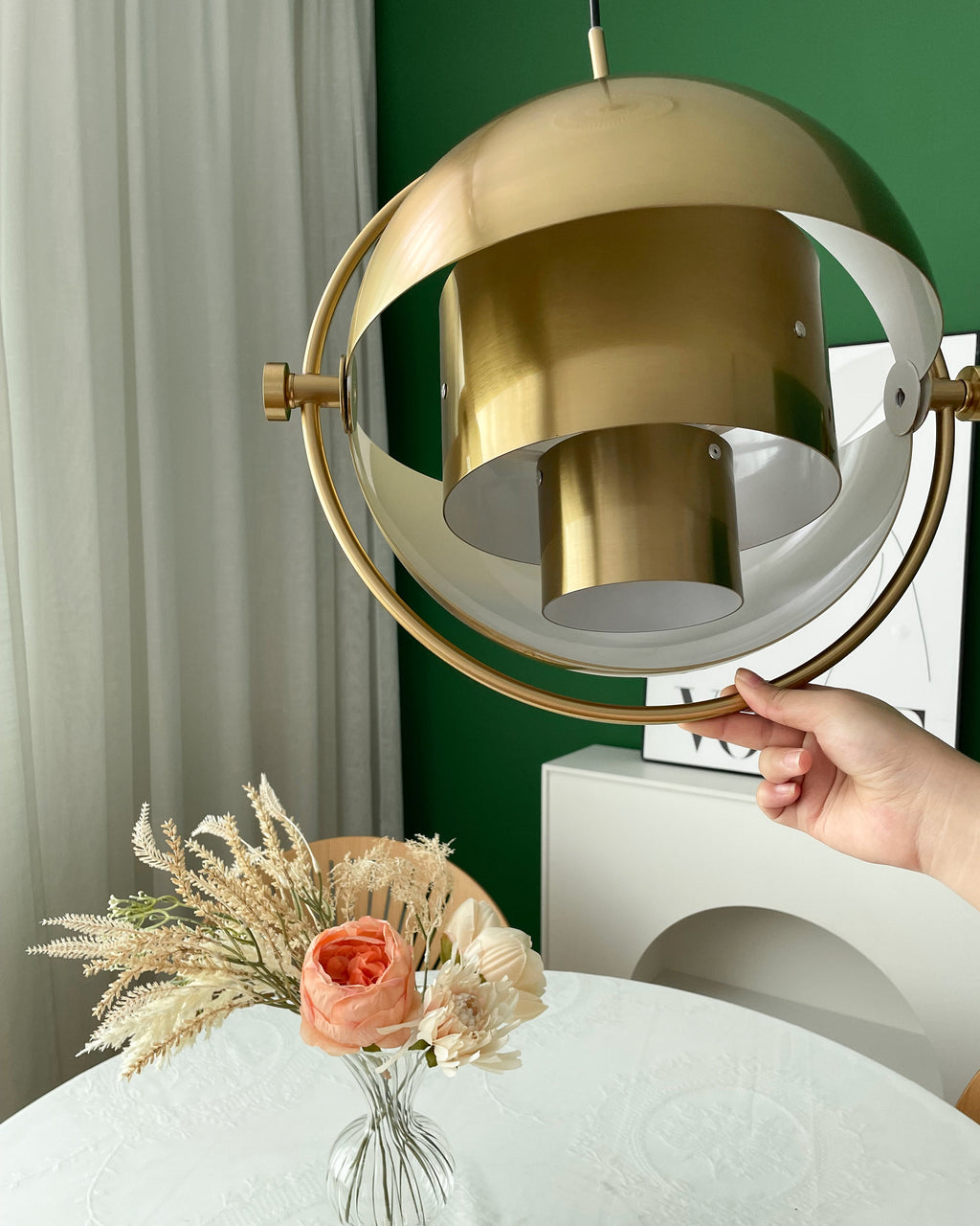 A hand holds the gold ring of this Clérachic pendant while the shade is swung open to show the inner layers.