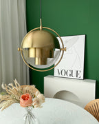 Gold-toned Clérachic pendant with its shade closed in the ring, above a round table and a poster on a green wall.