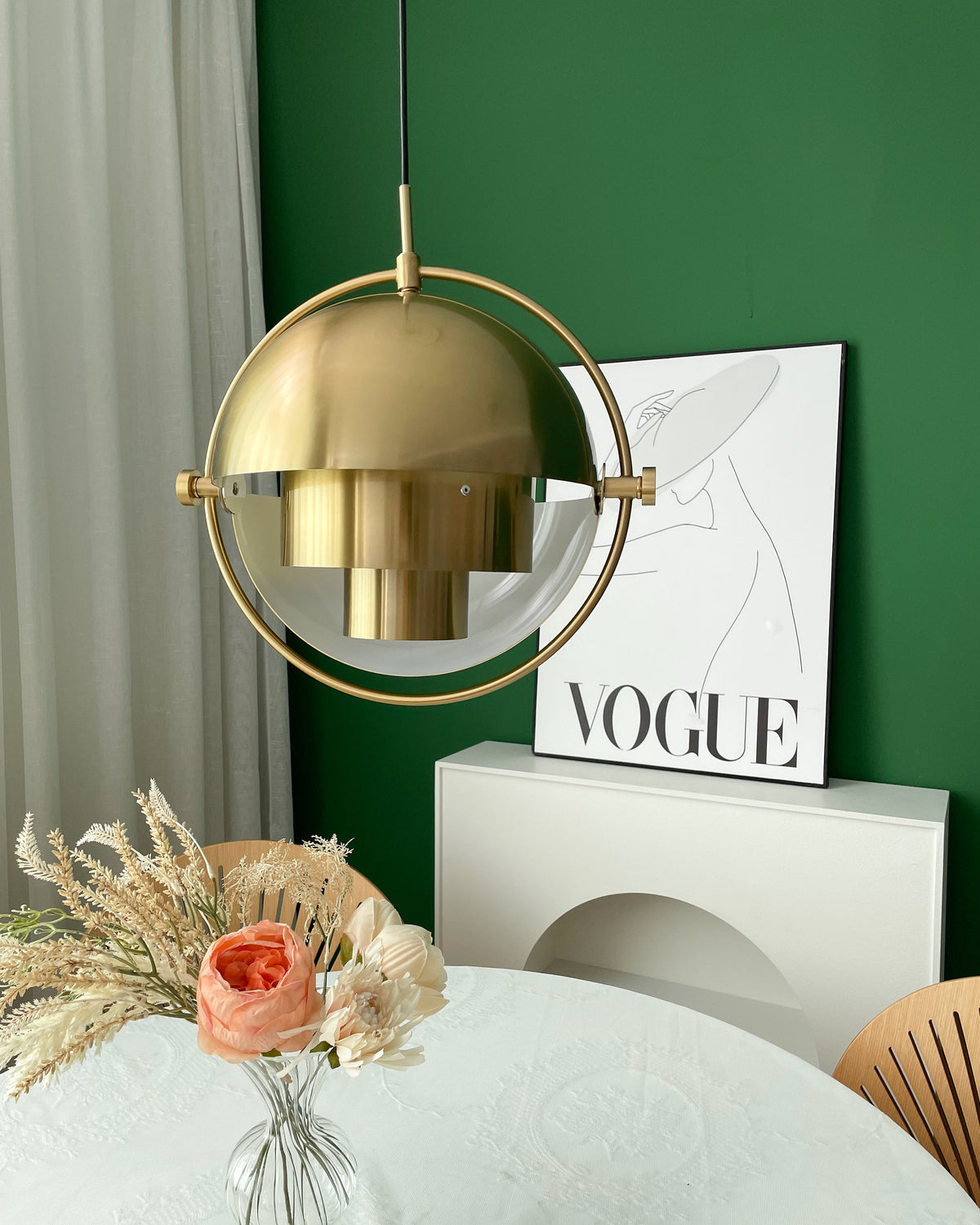 Gold-toned Clérachic pendant with its shade closed in the ring, above a round table and a poster on a green wall.
