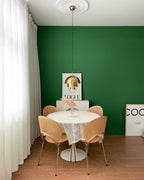 Gold-toned Clérachic pendant hung from a white ceiling rose above a round table with wooden chairs, in a green dining room.