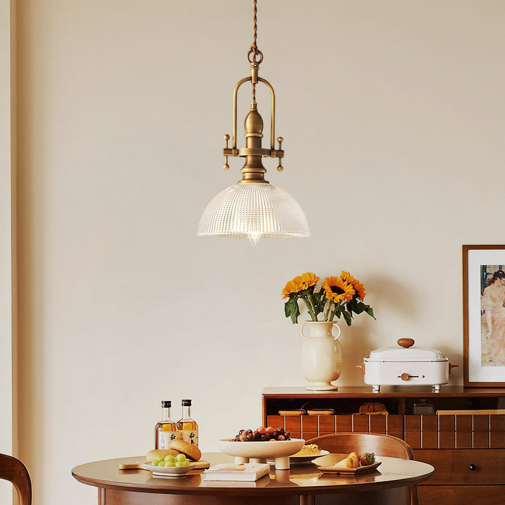 A Clérachic pendant with a ribbed glass dome hangs above a round wooden table, with sunflowers and a small sideboard behind.