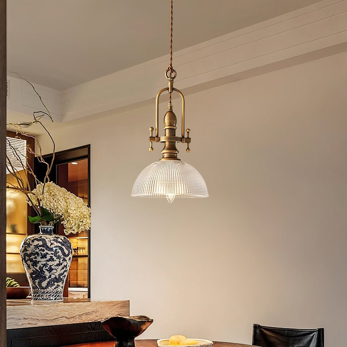 Clérachic glass pendant hanging in a dining corner, with a blue-and-white vase of hydrangeas and a stone-topped surface below.