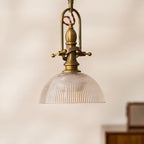 A Clérachic pendant with a clear ribbed dome, centred in a soft cream-toned frame with a small radio blurred behind.