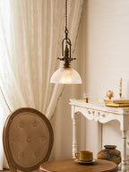 A Clérachic pendant hangs by a lace curtain, with a button-back chair, a white console and a small round table below.