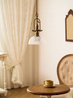 Clérachic pendant in a corner with a lace curtain, with the glass dome just lit above a table and a tufted chair.