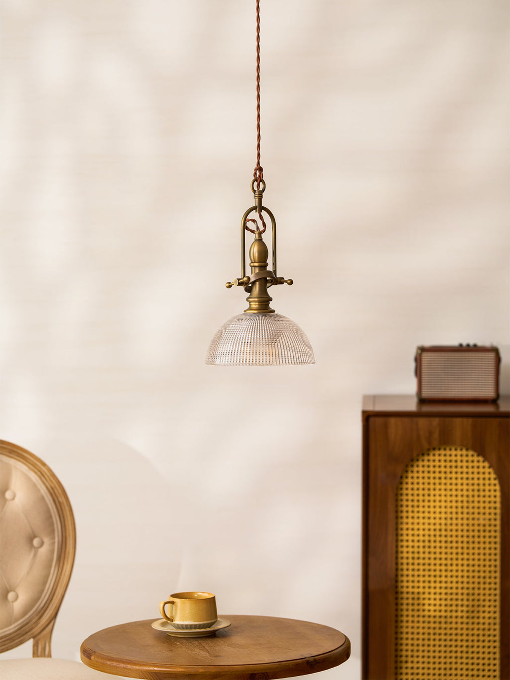 The Clérachic pendant seen from a distance, hanging above a wooden table and a cane-front cabinet on a pale wall.