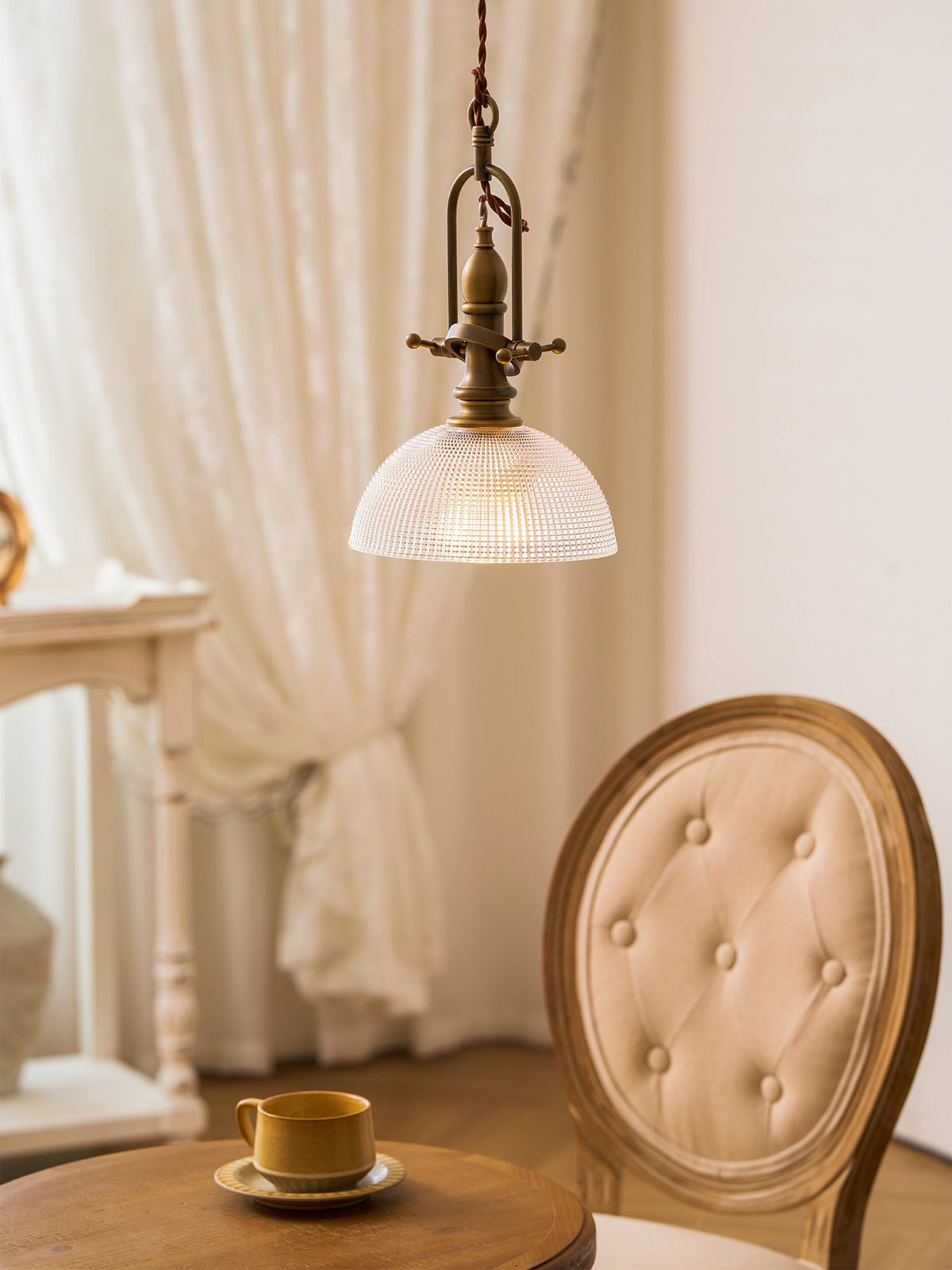 Clérachic pendant with a brass cradle and ribbed dome, hanging close to a lace curtain and a tufted chair.