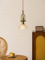 A Clérachic pendant on a pale wall, with a cane-panel cabinet and a mustard cup on a table below.