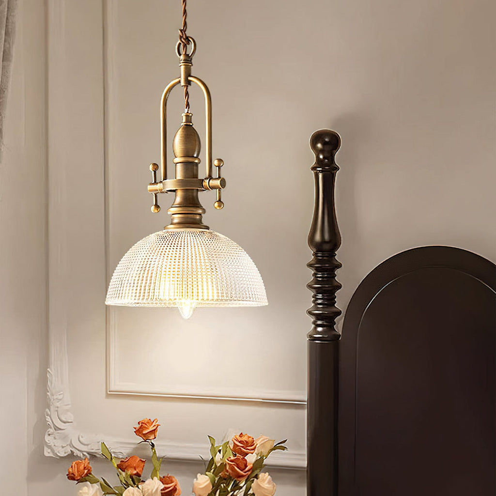 Lit Clérachic pendant beside a dark bedpost, with its ribbed glass dome and the bulb showing warm light.