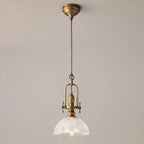 Clérachic pendant on a plain beige wall, with an antique brass canopy, a twisted brown cord and a clear ribbed dome.