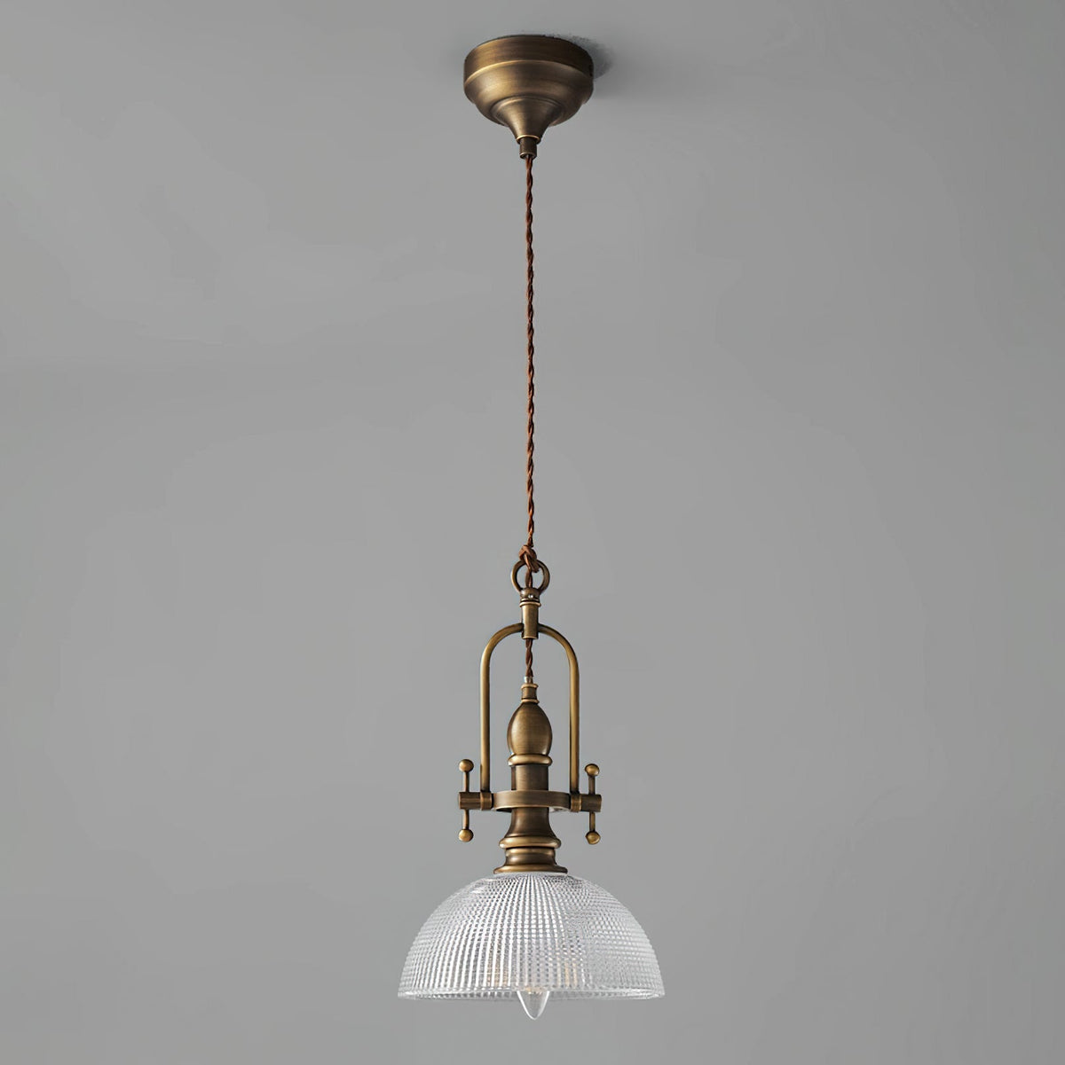 Clérachic pendant on a grey backdrop, with its antique brass canopy, a long twisted cord and a clear glass dome.