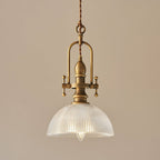 Clérachic pendant on a warm tan backdrop, with its brass frame and a ribbed glass dome lit around a filament bulb.